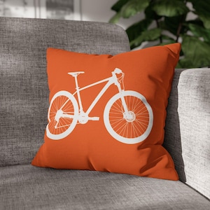 May include: Orange throw pillow with a white silhouette of a mountain bike.