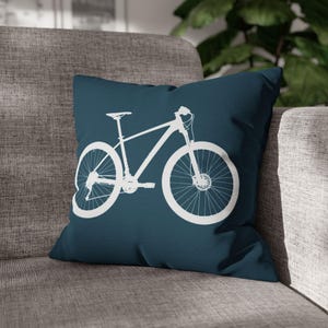 May include: A teal blue throw pillow with a white silhouette of a mountain bike. The bike has a curved handlebar and two wheels.