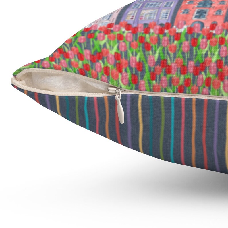 May include: A throw pillow with a zipper closure. The front of the pillow features a colorful striped pattern. The back of the pillow features a colorful illustration of houses and flowers.