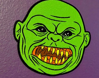 Puede incluir: Cara de monstruo verde con la boca abierta mostrando dientes afilados. El monstruo tiene una cara verde con ojos negros y un contorno negro.