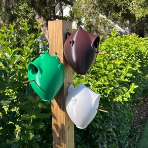Puede incluir: Tres casas para pájaros de diferentes colores: verde, marrón y blanco. Las casas para pájaros están unidas a un poste de madera.