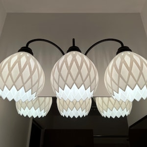 Puede incluir: Tres lámparas blancas con patrones geométricos y un marco de metal negro. Las lámparas tienen forma de flor con un diseño de celosía.