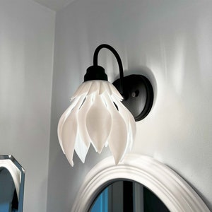 Puede incluir: Una lámpara blanca con forma de flor con detalles en metal negro. La lámpara está montada en una pared blanca.