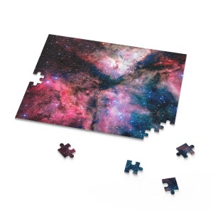 May include: A partially completed jigsaw puzzle featuring a colourful nebula image. The puzzle pieces are scattered around the main image, which shows a pink and blue nebula with stars.