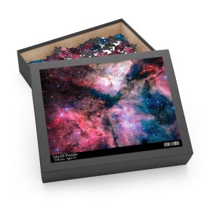 May include: A 500 piece jigsaw puzzle featuring a colourful nebula with pink, blue, and purple hues. The puzzle box is black with a white label that reads "16x20 Puzzle 500 pcs Ages 9+"