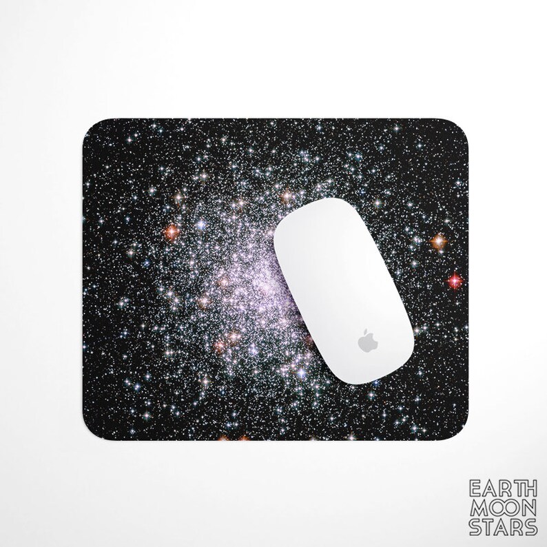 May include: A rectangular mousepad featuring a vibrant image of a galaxy with numerous stars in shades of white, pink, and orange against a black background. A white computer mouse with the Apple logo rests on the pad. The words "EARTH MOON STARS" are printed in white.