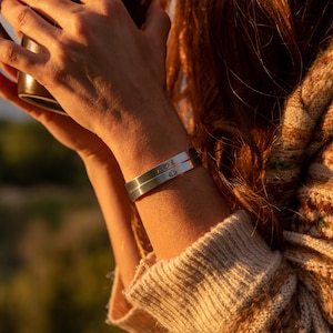 May include: A silver cuff bracelet with the inscription "M❤E" on one side and a small heart on the other side.