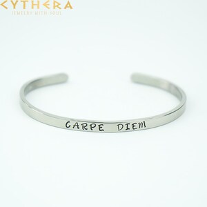 Pode incluir: Pulseira de bracelete de prata com a inscrição "Carpe Diem" gravada na frente.