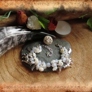 Könnte beinhalten: Ein silbernes Armband mit weißen und blauen Steinen, silbernen Anhängern und einer silbernen Kette. Das Armband liegt auf einer grauen Steinoberfläche.