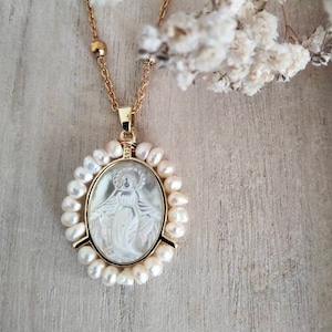 May include: A gold chain necklace with a white oval pendant featuring a religious image of the Virgin Mary. The pendant is surrounded by a circle of white pearls.