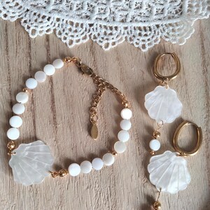 May include: A set of white shell jewelry with gold accents. The set includes a bracelet, a pair of earrings, and a necklace. The jewelry is made of white shell beads and gold chain.
