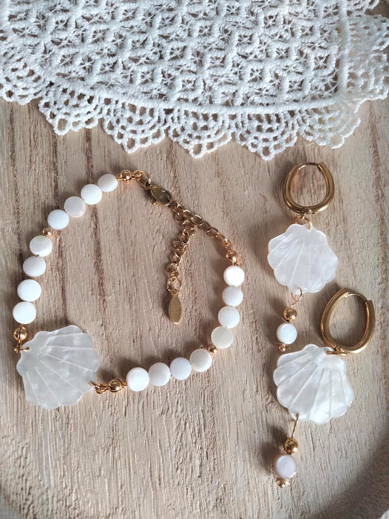 May include: A set of white shell jewelry with gold accents. The set includes a bracelet, a pair of earrings, and a necklace. The jewelry is made of white shell beads and gold chain.