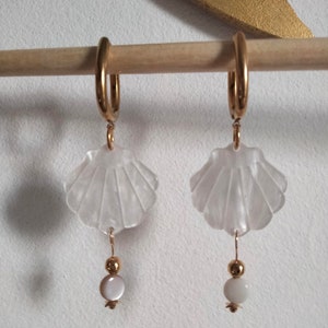 May include: A pair of gold hoop earrings with a white seashell charm and a white pearl bead dangling from each hoop.