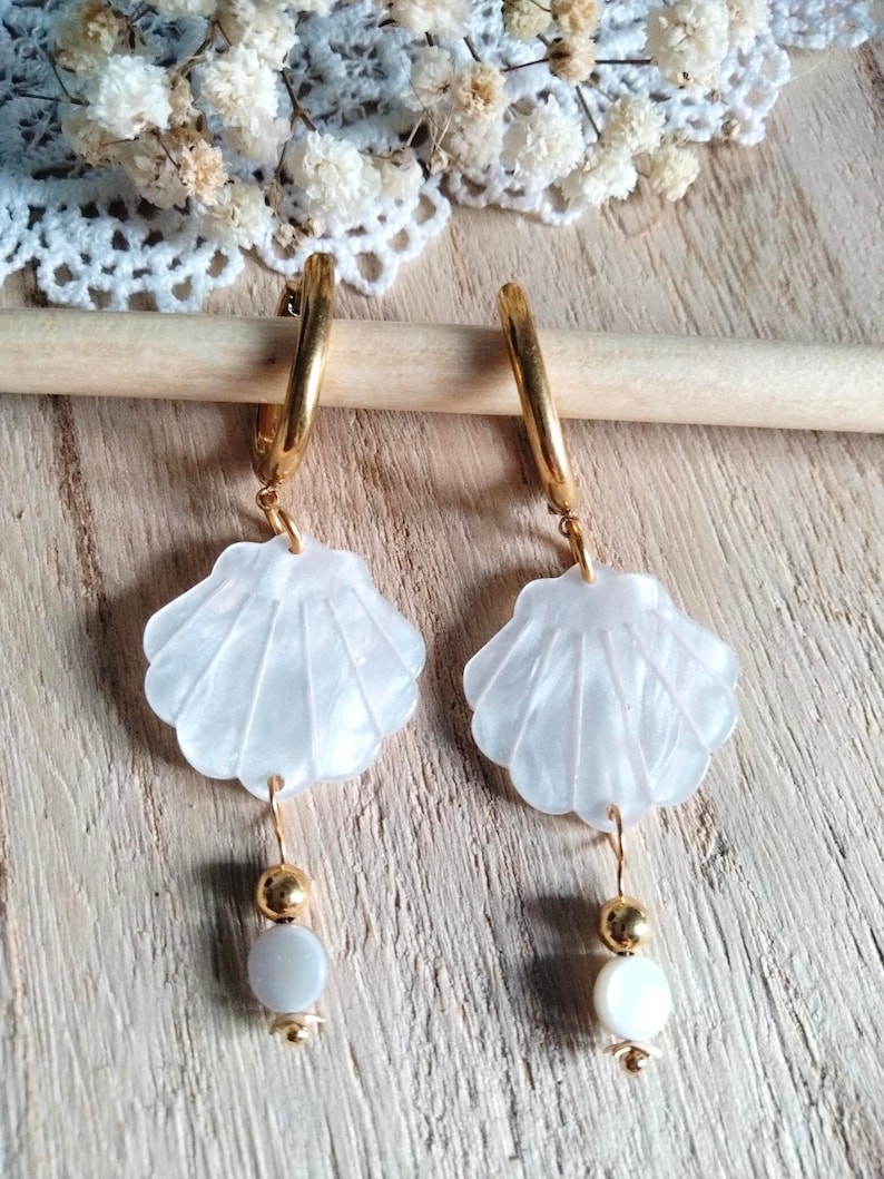 May include: Gold hoop earrings with white shell charms and white pearl accents.