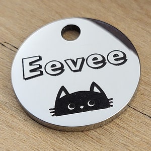 Peut inclure: Une médaille d'identification pour animal de compagnie en argent avec le nom "Eevee" gravé en lettres noires et une silhouette de chat noir avec des yeux blancs.