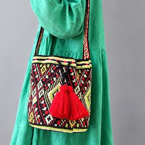 Woman wearing a handmade Ukrainian folk crochet shoulder bag with red tassels and geometric pattern.