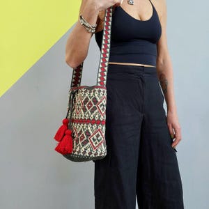May include: A red, white, and green crocheted bag with tassels. The bag has a geometric pattern and is worn over the shoulder.