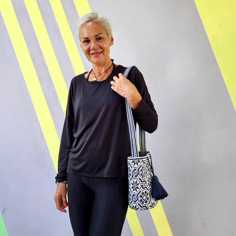 May include: A white and navy blue patterned tote bag with a navy blue tassel. The bag has a striped strap and is held over the shoulder. The bag's design features geometric shapes and floral patterns.