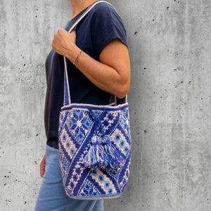 Large crochet bucket bag with Ukrainian folk pattern in blue and cream tones, handmade from recycled cotton yarn, boho shoulder tote with tassel drawstring closure, worn on shoulder, geometric embroidery inspired design, spacious handmade bag with traditional Ukrainian ornament, sustainable crochet handbag for everyday use.