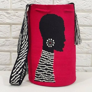 May include: A red crocheted bag with a black and white patterned strap. The bag features a silhouette of a person with a black and white patterned design and a red circle earring.