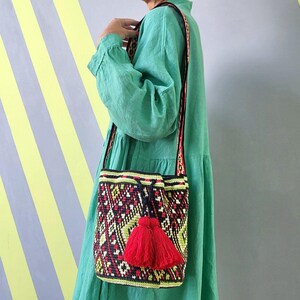 Woman wearing colorful crochet bucket bag with red tassels and long shoulder strap.