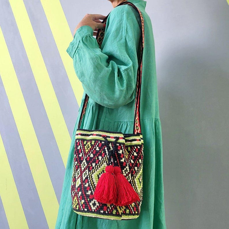 Woman wearing colorful crochet bucket bag with red tassels and long shoulder strap.