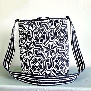 May include: A woven shoulder bag with a geometric pattern in navy blue and white. The bag has a rectangular shape with a matching striped strap. The strap is approximately 40 inches long. The bag is made of a durable material.