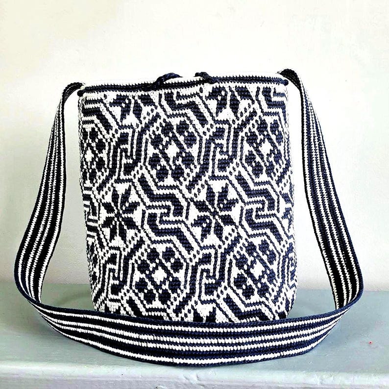 May include: A woven shoulder bag with a geometric pattern in navy blue and white. The bag has a rectangular shape with a matching striped strap. The strap is approximately 40 inches long. The bag is made of a durable material.