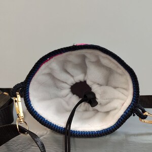 May include: A black and blue drawstring bag with a white fleece lining. The bag has a gold clasp and a black strap.
