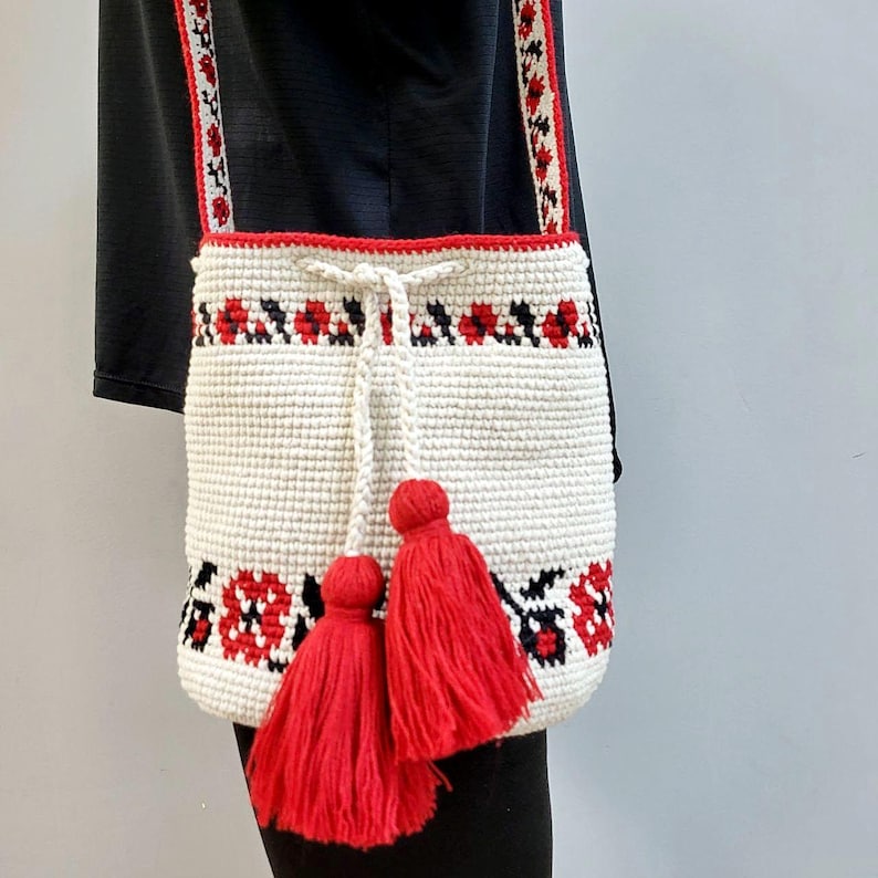 May include: White crocheted tote bag with red and black floral embroidery and red tassels. The bag has a long strap.