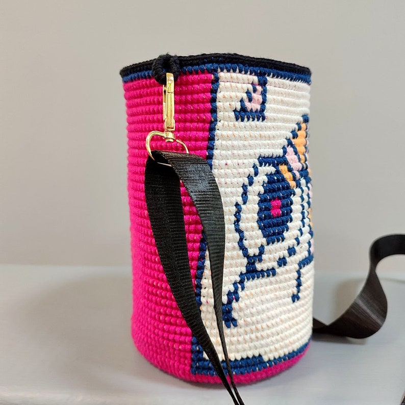May include: A pink and white crocheted bag with a black strap and a gold clasp. The bag features a colorful pixelated design of a cartoon animal.