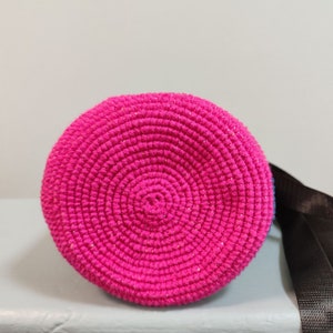 May include: A pink crocheted bag with a round bottom and a black strap.