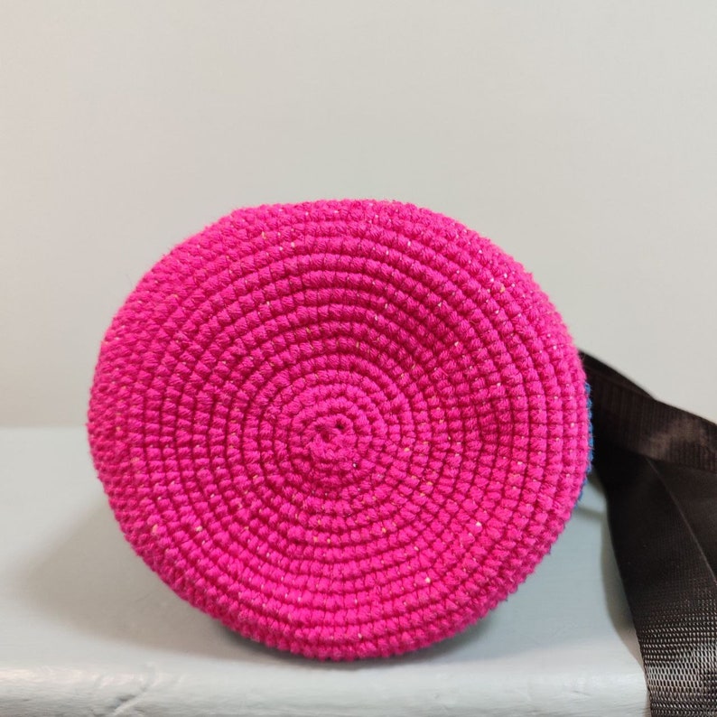 May include: A pink crocheted bag with a round bottom and a black strap.
