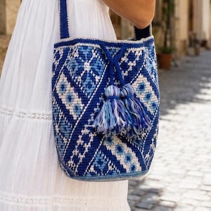 Blue crochet bucket bag with Ukrainian-inspired geometric pattern on woman in white summer dress