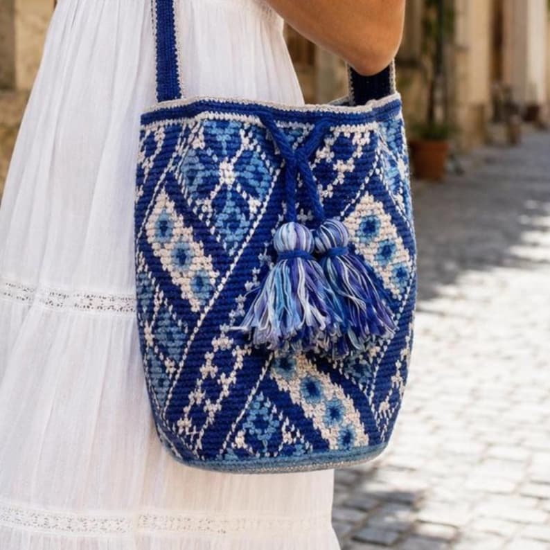 Blue crochet bucket bag with Ukrainian-inspired geometric pattern on woman in white summer dress