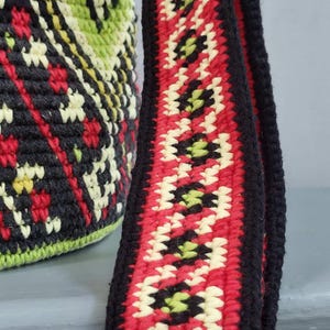 Close up of handmade woven shoulder strap with red, cream, green and black geometric pattern.