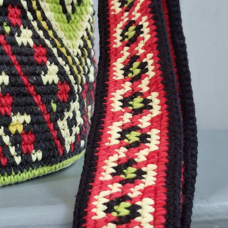 Close up of handmade woven shoulder strap with red, cream, green and black geometric pattern.