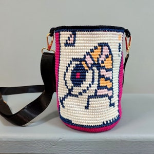 May include: A white crocheted bag with a pink trim and a black strap. The bag features a colorful cartoon design of a tiger and a bear.