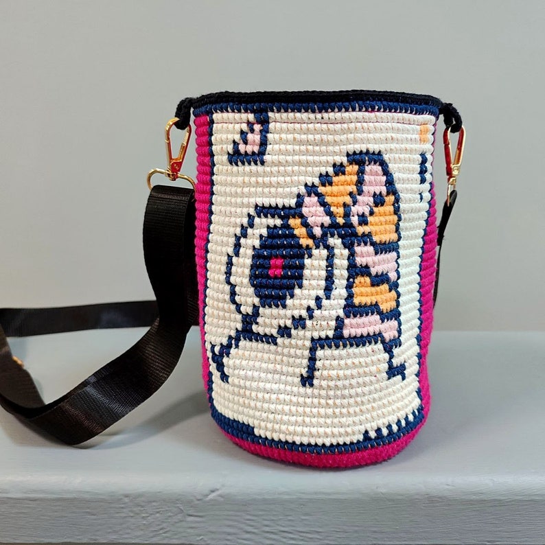 May include: A white crocheted bag with a pink trim and a black strap. The bag features a colorful cartoon design of a tiger and a bear.