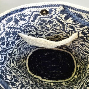 May include: A handmade, open-top tote bag with a geometric pattern in navy blue and white. The bag features a white pocket and a magnetic snap closure. The interior is a solid navy blue, and the bag is made of a woven material.