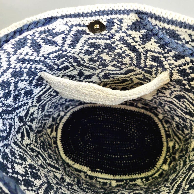 May include: A handmade, open-top tote bag with a geometric pattern in navy blue and white. The bag features a white pocket and a magnetic snap closure. The interior is a solid navy blue, and the bag is made of a woven material.