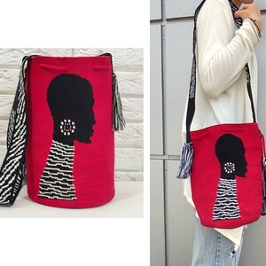 May include: A red woven bag with a black and white silhouette of a person's head with a large earring. The bag has a black and white striped strap and black and white tassels.