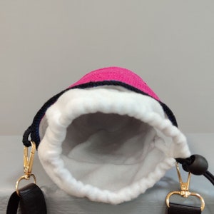 May include: A pink drawstring bag with a white lining and black straps. The bag has a gold metal clasp and a black toggle.