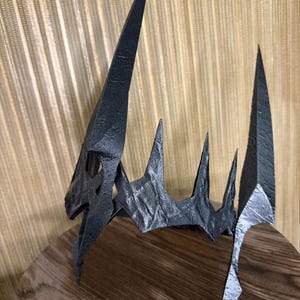 May include: A black, 3D printed crown with a sharp, pointed design. The crown has a textured surface and is made of a durable material.