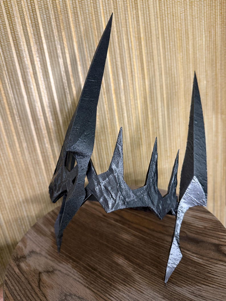 May include: A black, 3D printed crown with a sharp, pointed design. The crown has a textured surface and is made of a durable material.