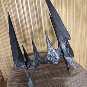May include: A black, jagged crown with a textured surface. The crown is made of a hard material and has a sharp, pointed design.