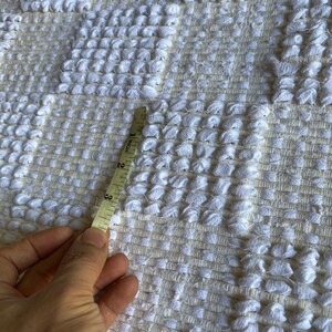 Pode incluir: Close-up de um tapete branco tecido com uma superf&iacute;cie texturizada. Uma fita m&eacute;trica &eacute; colocada no tapete, mostrando 3 polegadas.