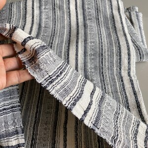 May include: Close-up of a white and black striped fabric with a textured weave. The fabric has a subtle sheen and a slightly rough texture.