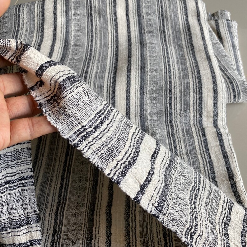 May include: Close-up of a white and black striped fabric with a textured weave. The fabric has a subtle sheen and a slightly rough texture.
