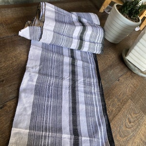 May include: White and black striped fabric with a woven texture. The fabric is folded in half and has a black border.